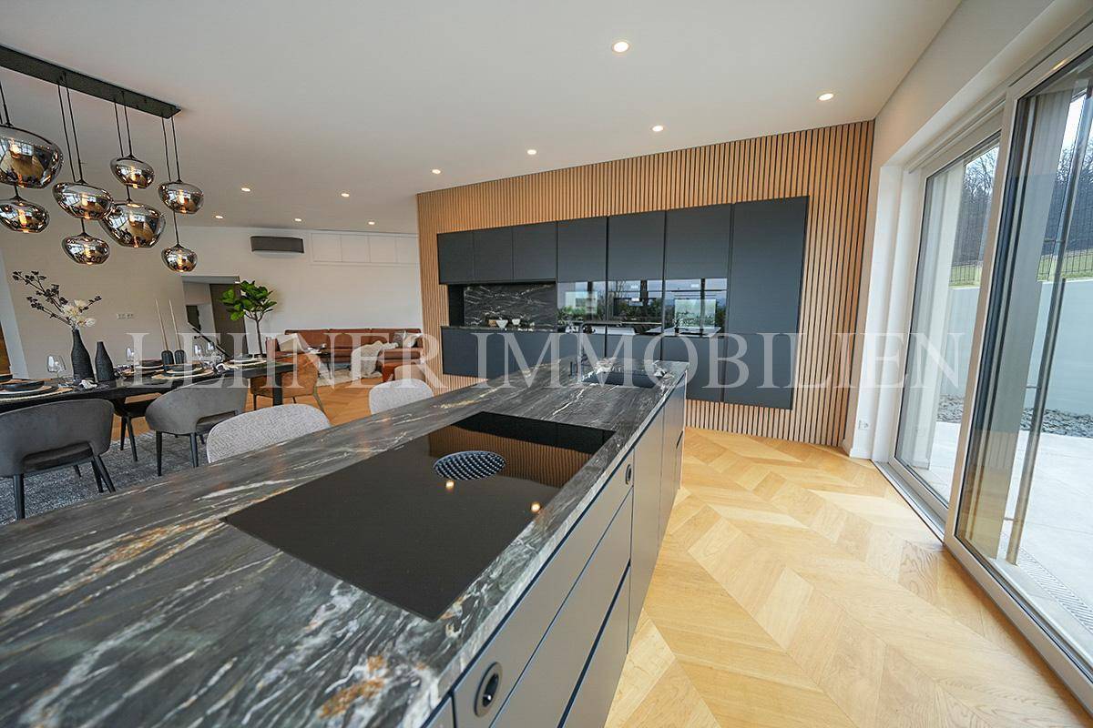 Offene Küche mit Kochinsel, Induktionskochfeld und Zugang zur Terrasse, verbunden mit Essbereich.