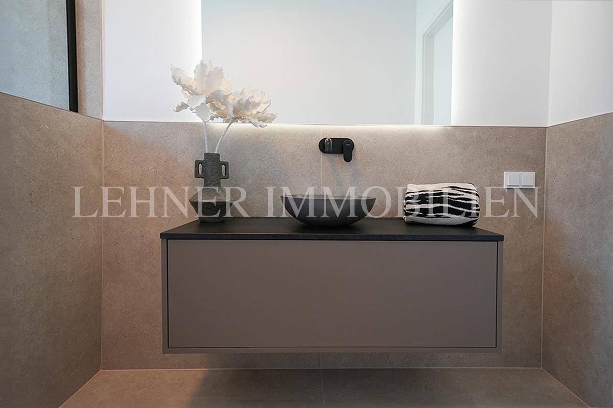 Eleganter Waschtisch mit Aufsatzwaschbecken, schwarzer Armatur und beleuchtetem Spiegel im modernen Bad.