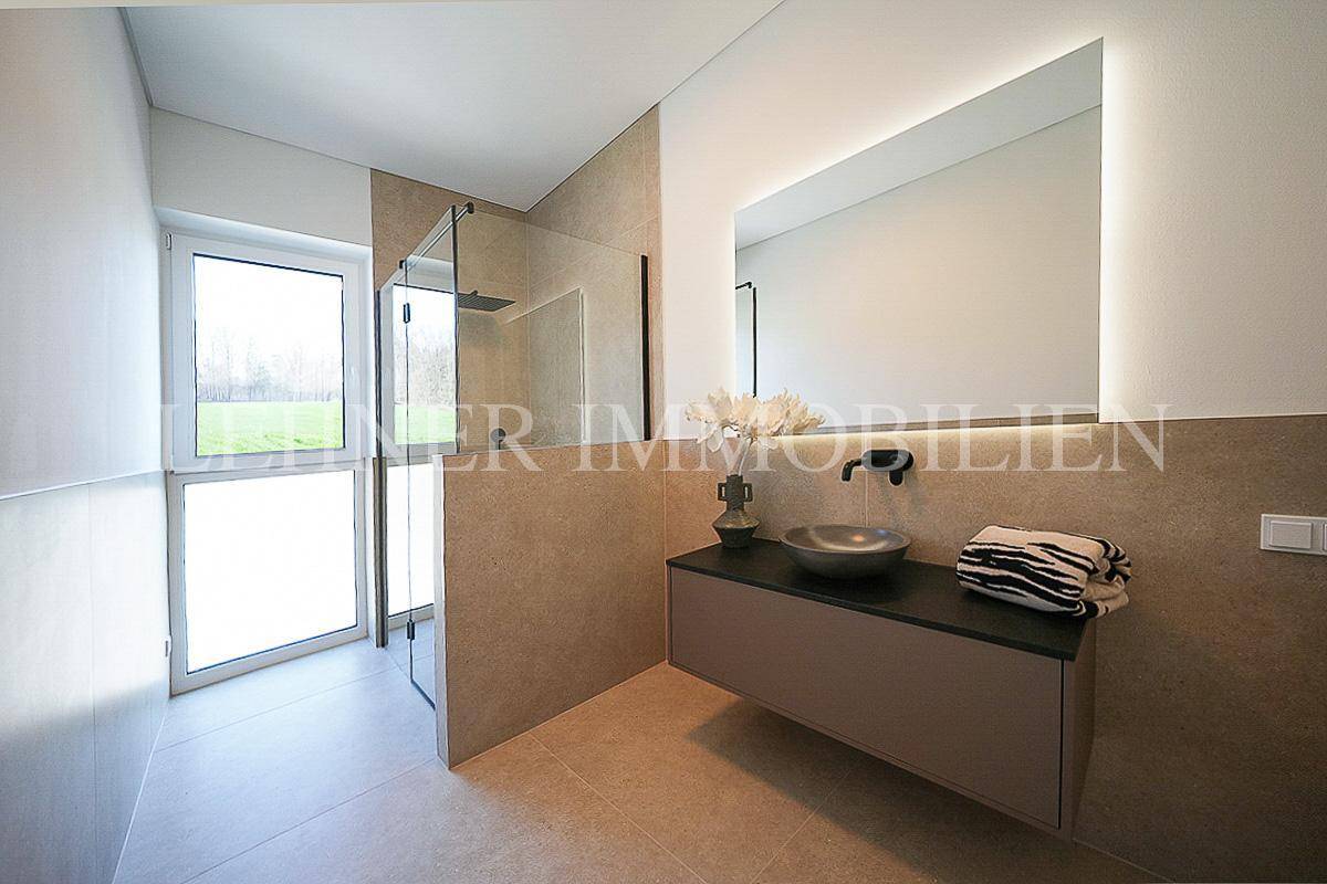 Modernes Badezimmer mit begehbarer Dusche, elegantem Waschtisch und großem beleuchteten Spiegel.