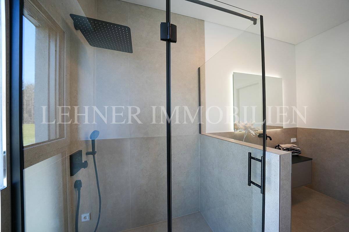 Detailansicht der modernen begehbaren Dusche mit Regenduschkopf und schwarzen Armaturen im Badezimmer.