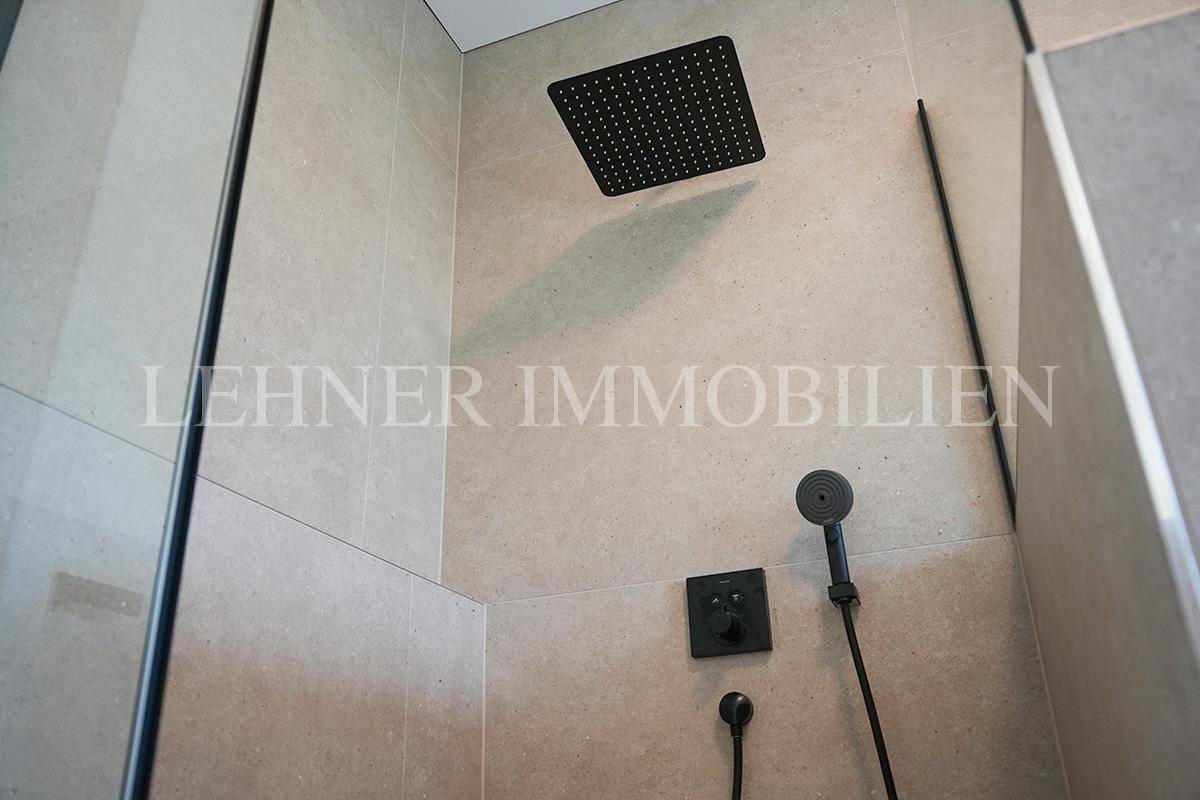 Detailansicht der modernen Regendusche mit schwarzem Duschkopf und Handbrause in der begehbaren Dusche.