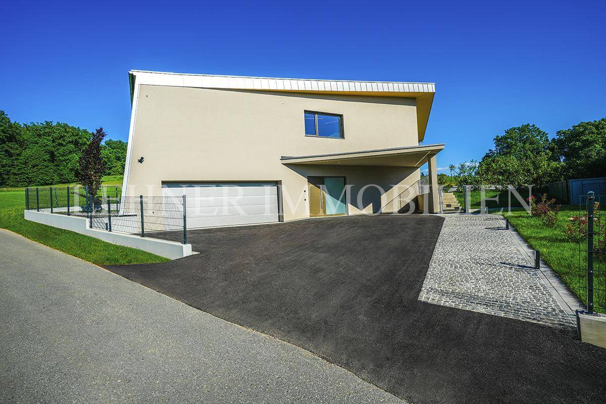 Vorderansicht des modernen Hauses mit integrierter Garage, Carport und gepflasterter Zufahrt.