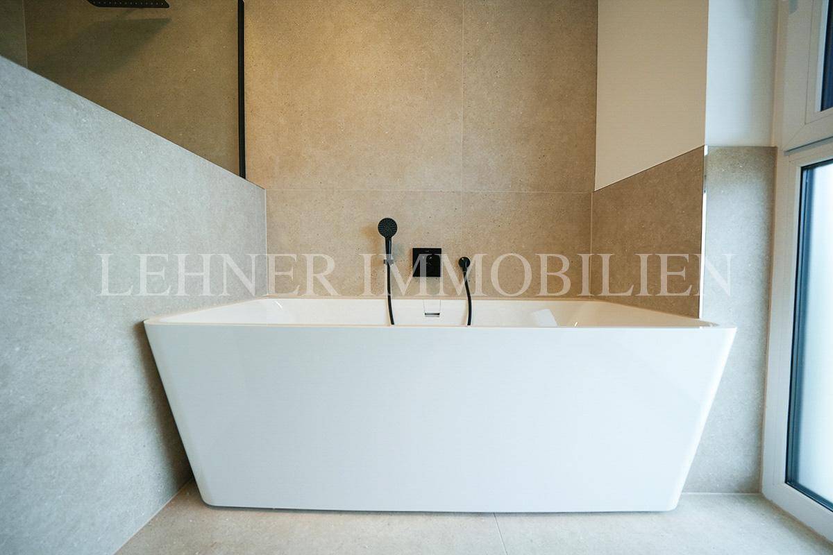 Elegante freistehende Badewanne mit schwarzen Armaturen in einem modernen, hell gefliesten Badezimmer.
