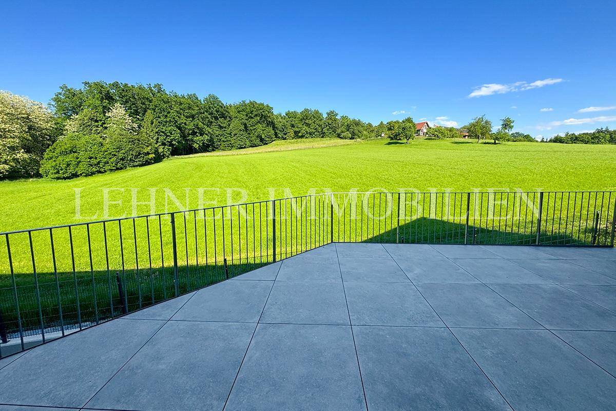 Große geflieste Terrasse mit Metallgeländer und weitem Blick ins Grüne.