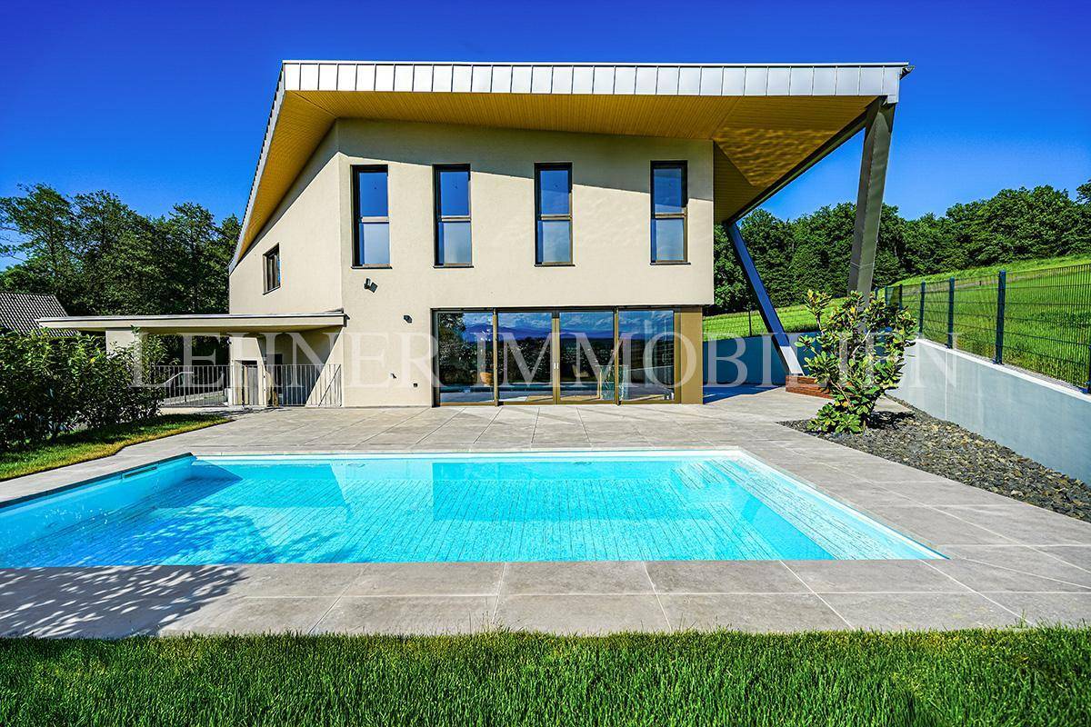 Zeitgenössisches Haus mit großem Pool und gepflegtem Rasen, umgeben von grüner Natur und klarem Himmel.