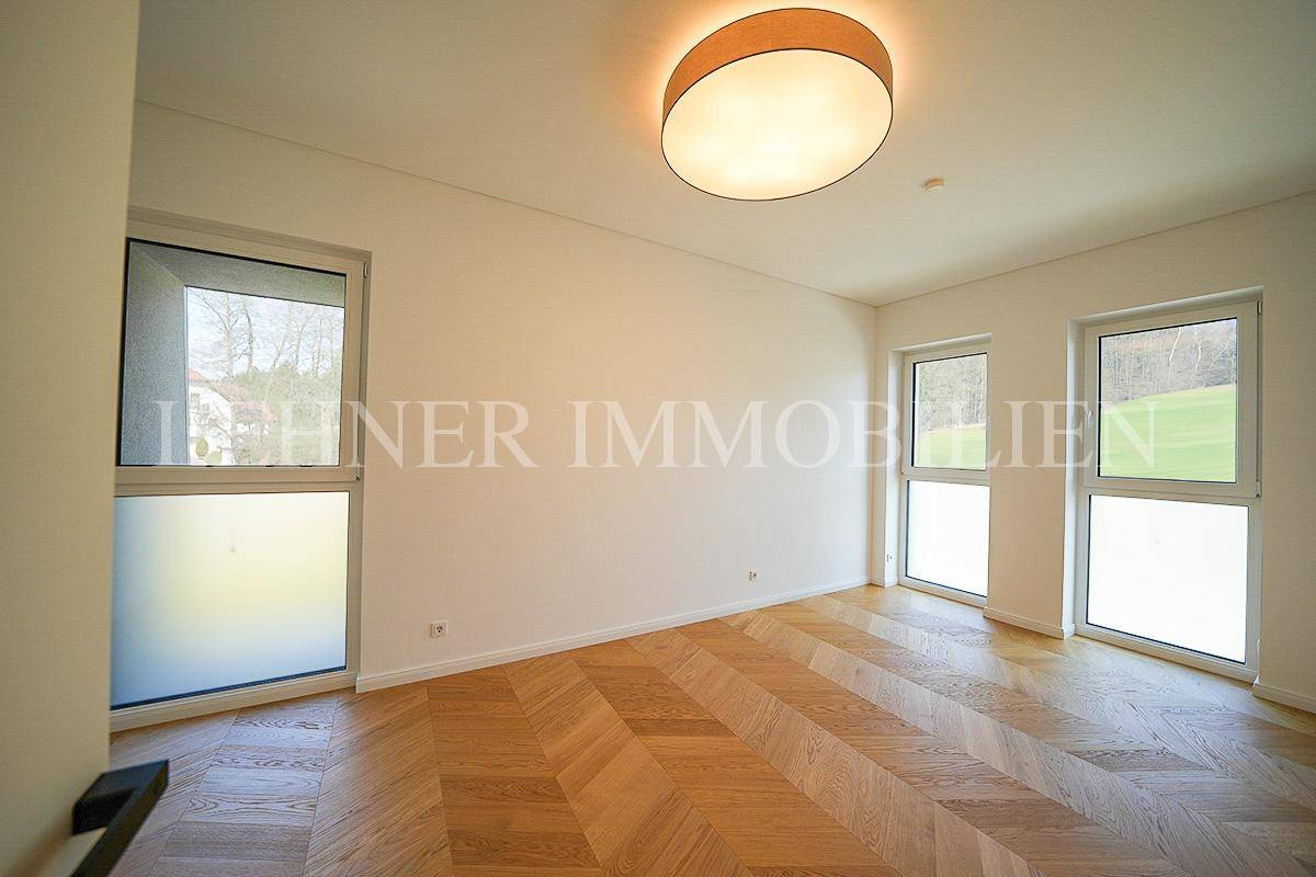 Lichtdurchflutetes Zimmer mit modernem Fischgrätparkett und Blick ins Grüne durch große Fenster.