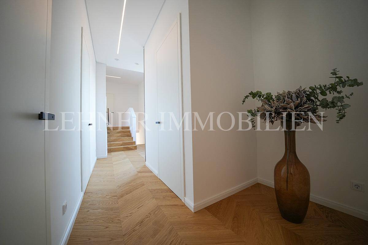 Heller Flur mit Fischgrätparkett, integrierten Schränken und moderner Deckenbeleuchtung, führt zur Treppe.