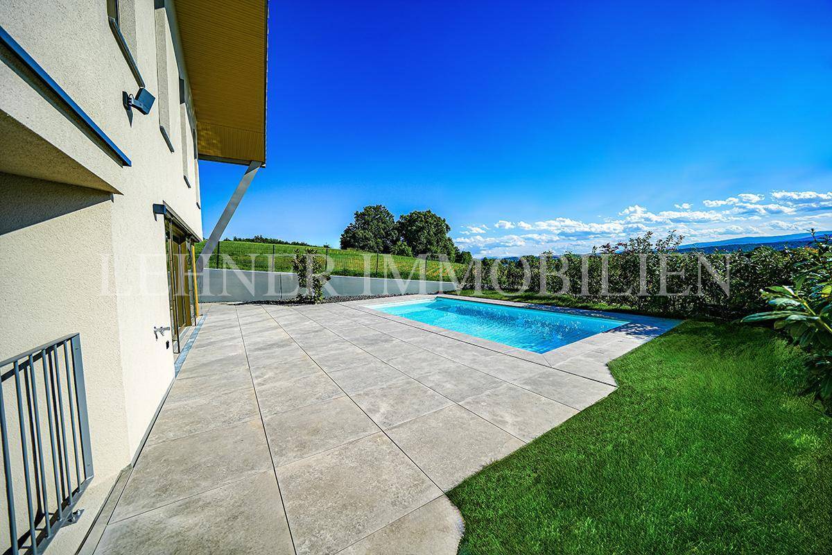 Geräumige geflieste Terrasse neben dem Haus mit Blick auf den Pool und die umliegende grüne Landschaft.
