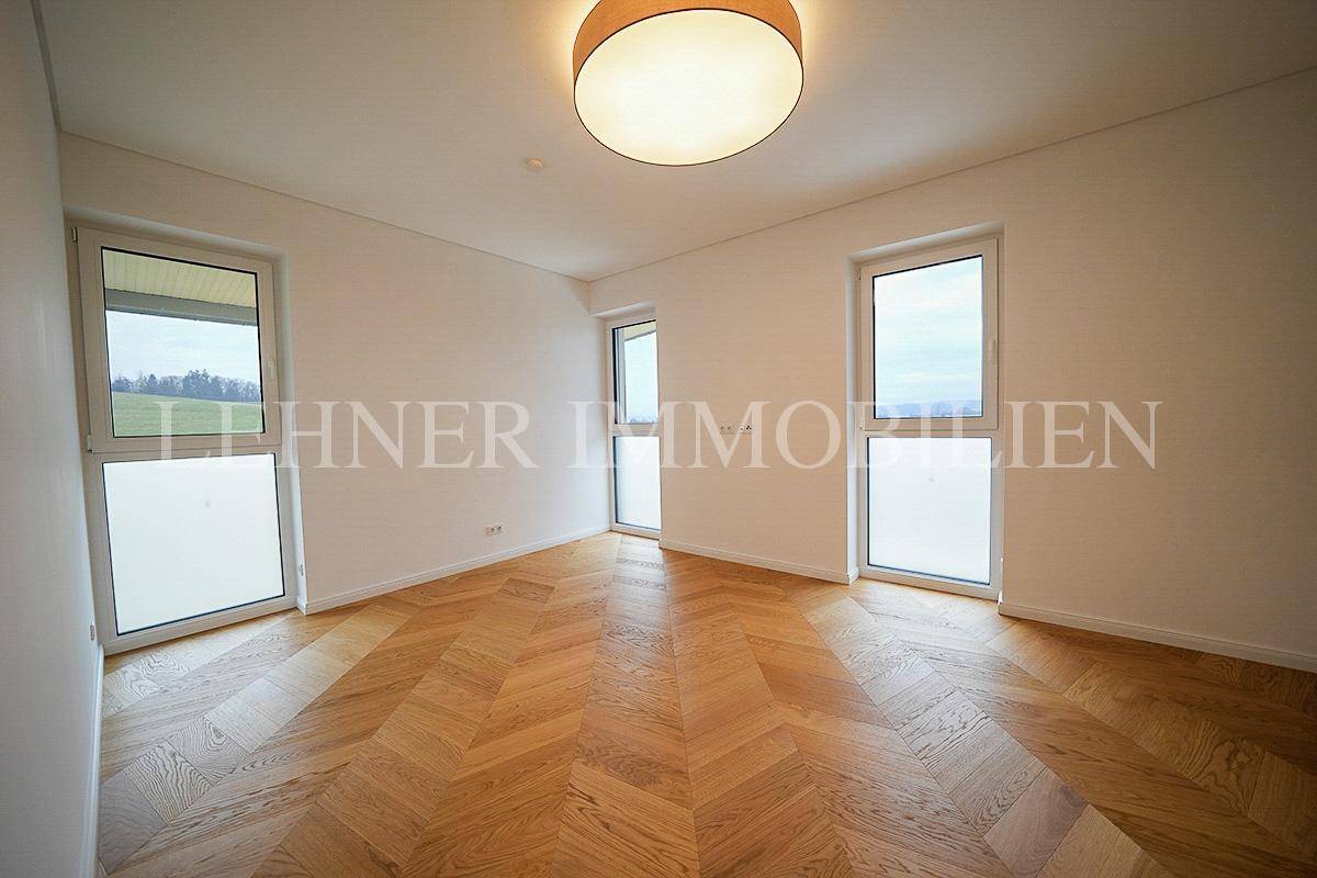 Geräumiges Zimmer mit elegantem Fischgrätparkett und viel Tageslicht durch mehrere Fenster.