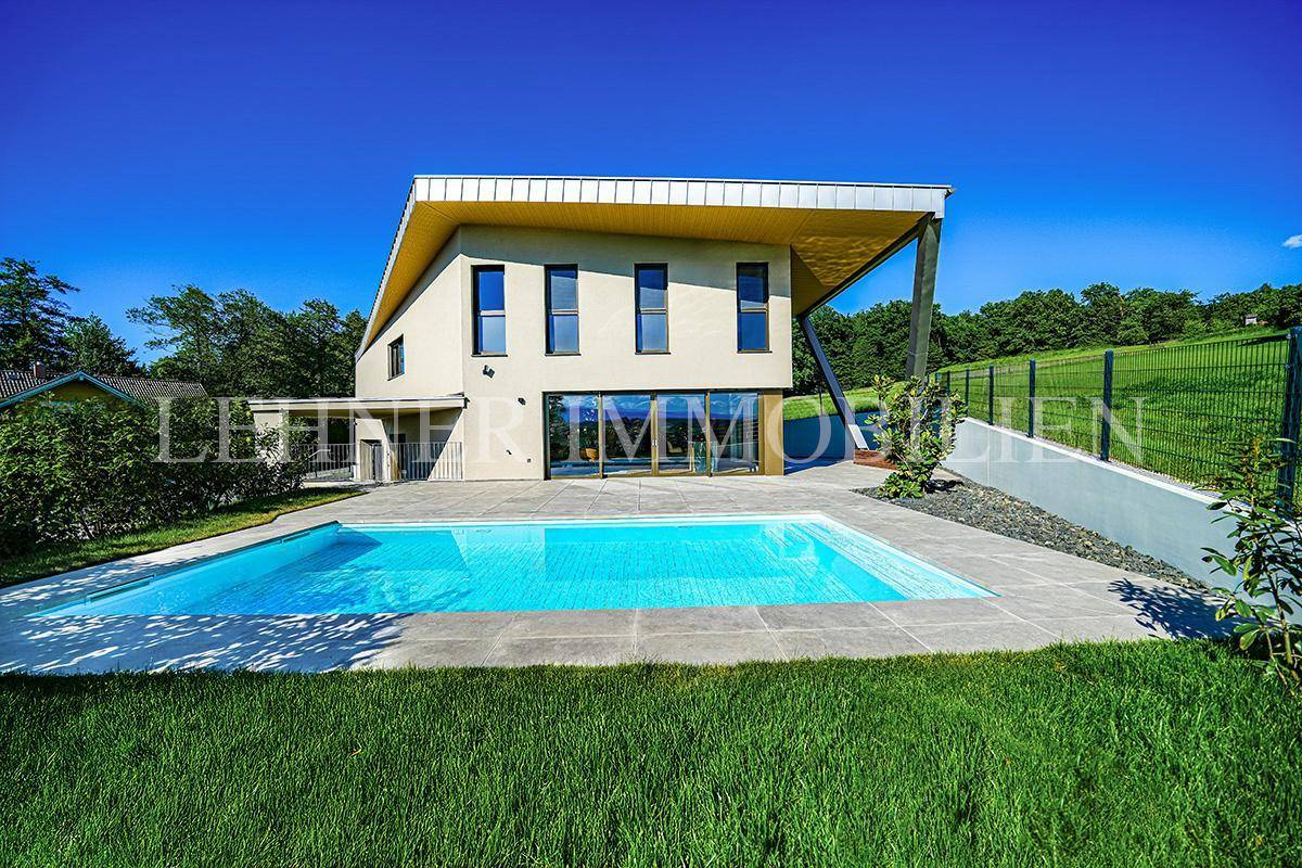 Modernes Einfamilienhaus mit Swimmingpool und weitläufigem Gartenbereich unter strahlend blauem Himmel.