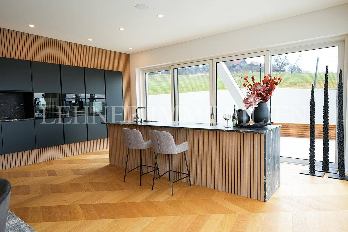 Moderne Küche mit Kücheninsel, schwarzen Fronten und Holzakzenten, mit Zugang zur Terrasse.