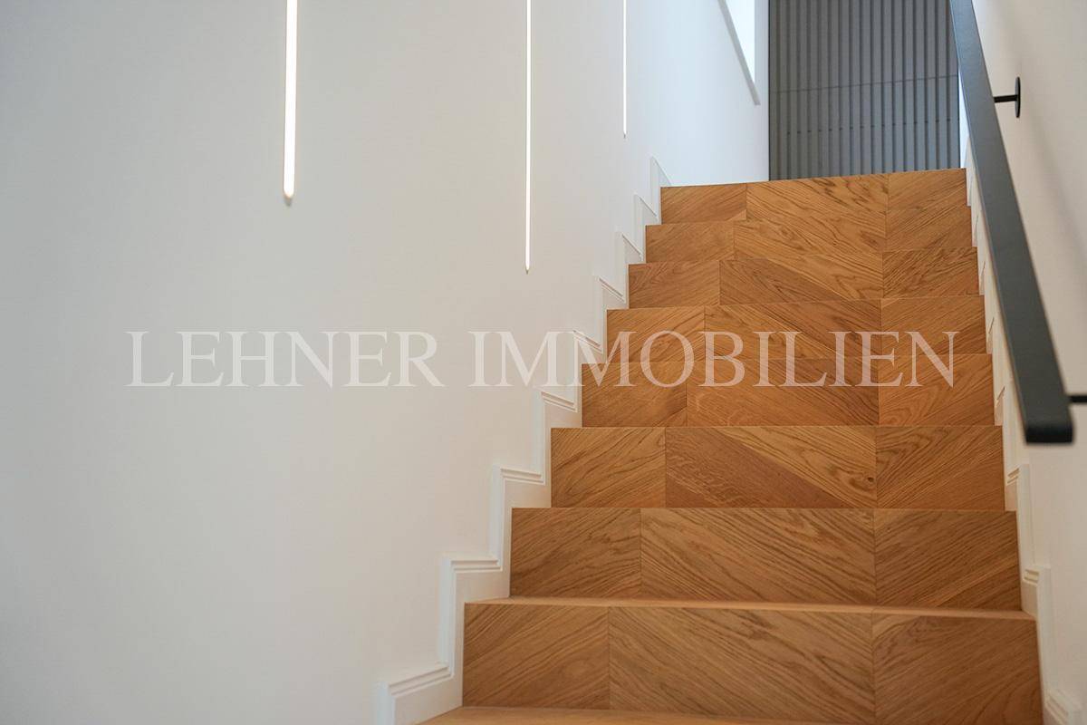 Holztreppe mit Fischgrätmuster und indirekter Beleuchtung an der Wand.