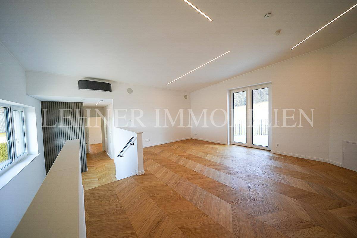 Geräumiger Wohnbereich im Obergeschoss mit Parkettboden, großen Fenstern und Zugang zum Balkon.