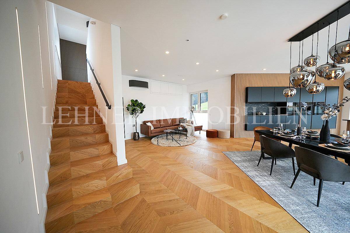 Großzügiger Wohnbereich mit offener Küche, Essbereich und moderner Holztreppe, die das Design ergänzt.