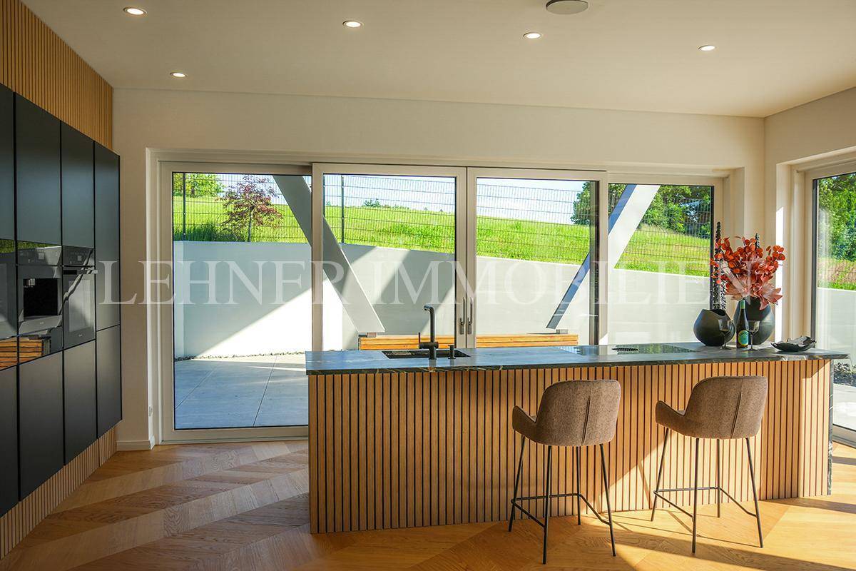 Helle moderne Küche mit Kücheninsel und Blick auf die grüne Landschaft durch große Fenster.