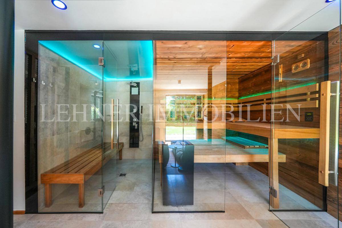 Exklusiver Wellnessbereich mit Glas-Sauna, Dusche und Holzbänken auf hellem Fliesenboden.