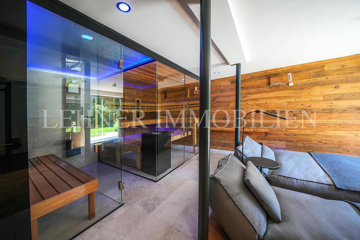 Moderner Wellnessbereich mit Glas-Sauna und komfortablen Liegen auf Fliesenboden.