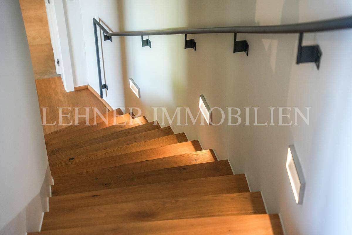 Moderne Holztreppe mit integrierter Wandbeleuchtung und schwarzem Handlauf.
