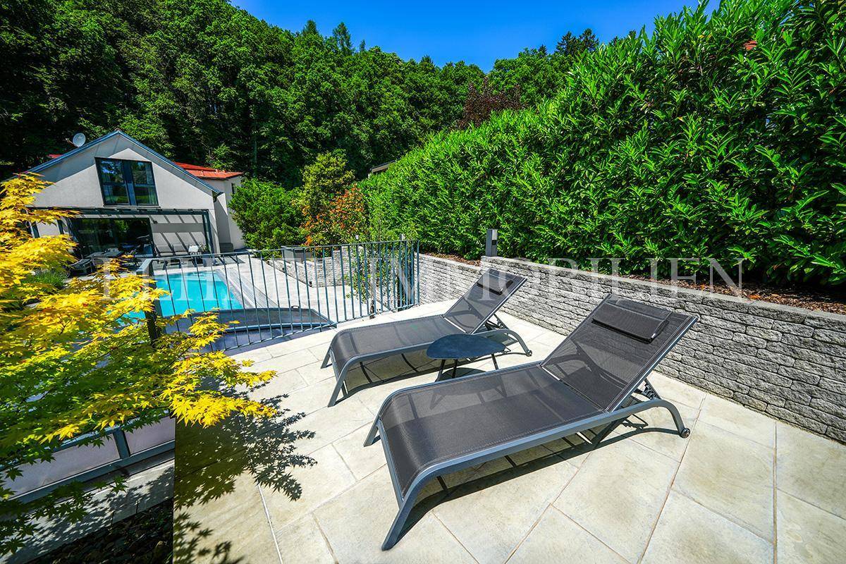 Entspannungsbereich mit Sonnenliegen auf der Terrasse, umgeben von viel Grün und Blick auf das Haus.