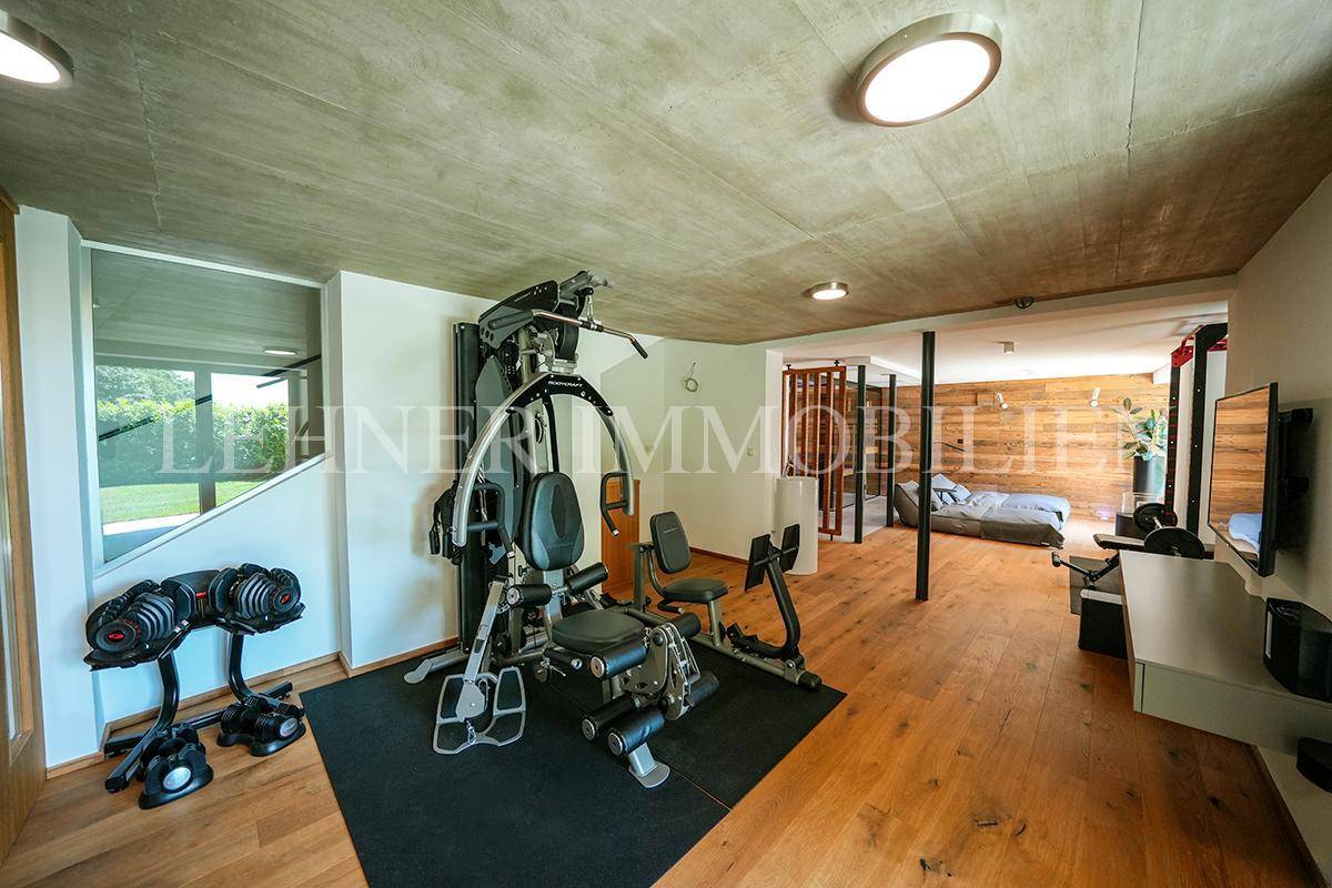 Moderner Fitnessraum mit Trainingsgeräten, Holzboden und Lounge-Bereich im Hintergrund.