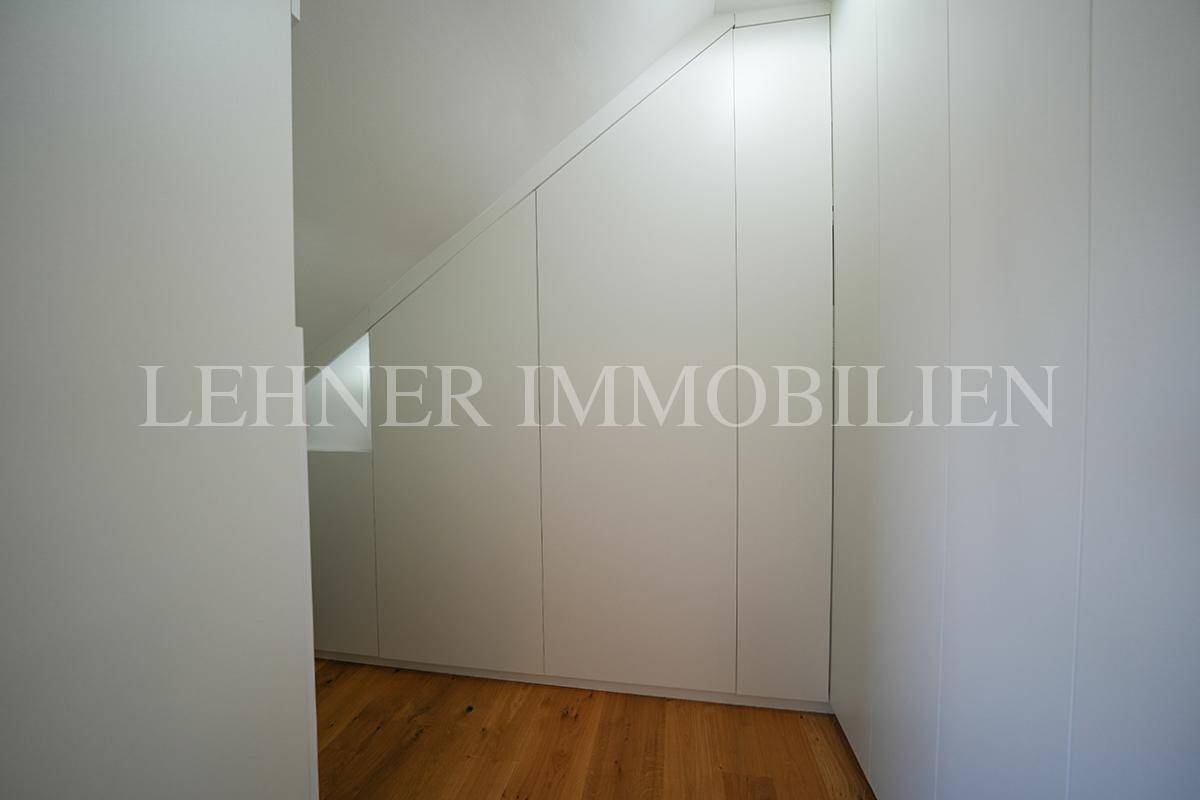 Funktionaler Ankleidebereich mit maßgefertigten Einbauschränken, Holzboden und Dachschräge.