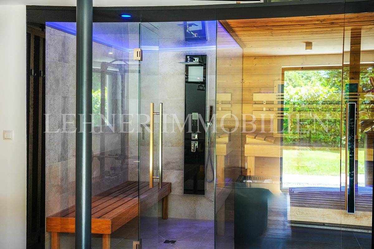 Moderne Duschkabine im Wellnessbereich mit Glaswänden, Duschpaneel und Holzbank.