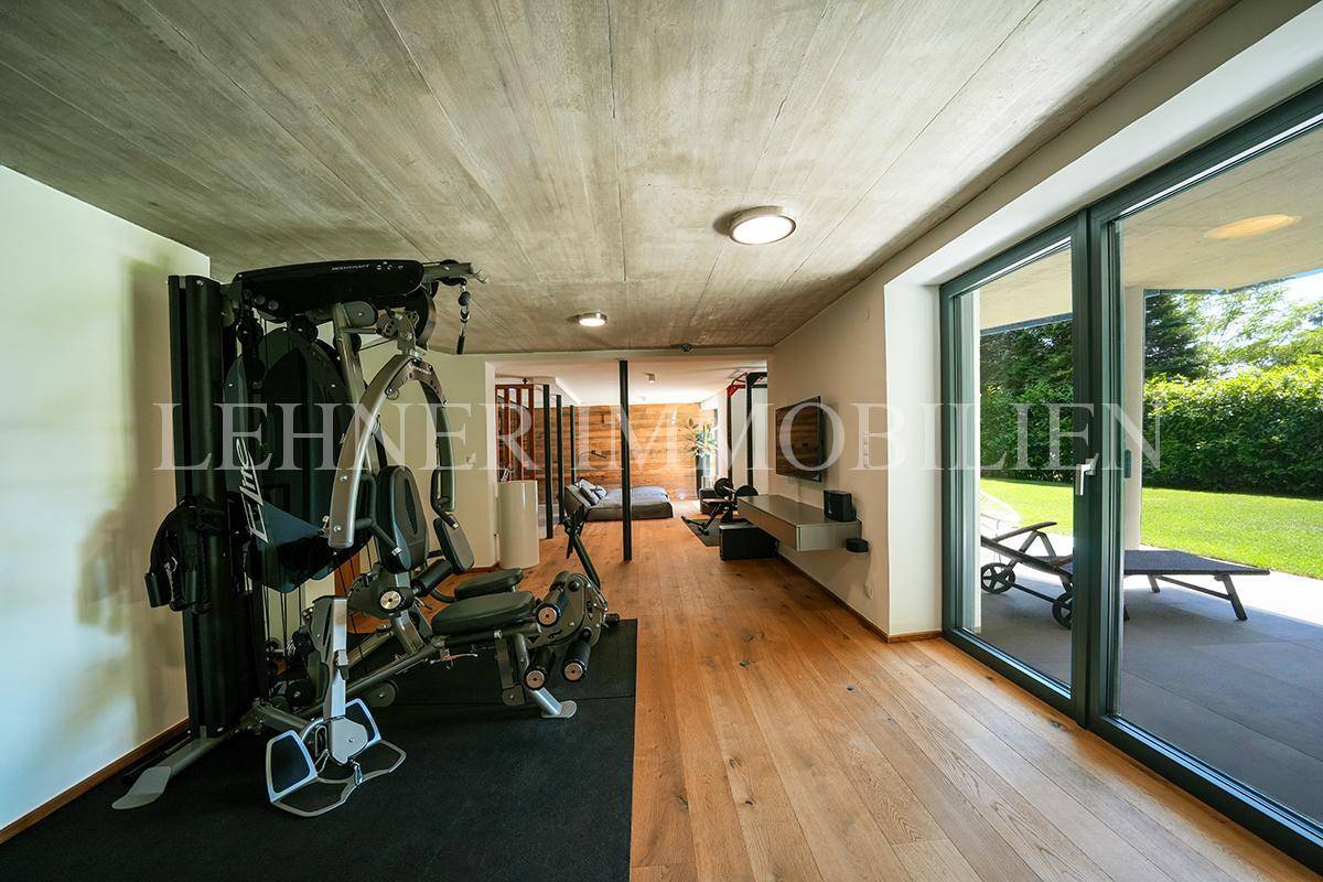 Geräumiger Fitnessbereich mit Holzboden und großen Glasfronten zum Garten.