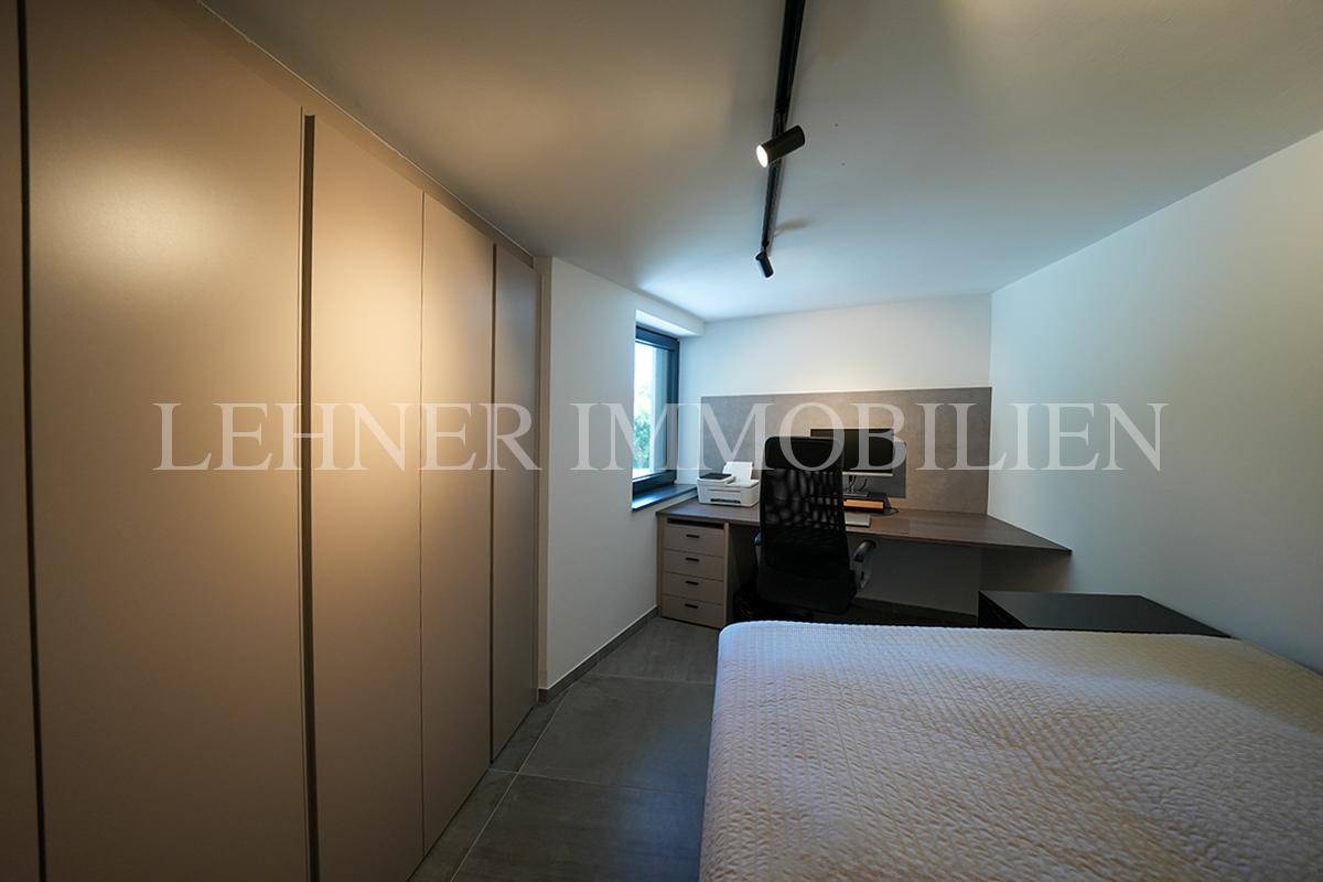 Schlafzimmer mit Einbauschränken, Schreibtisch und Fenster, auf Fliesenboden.