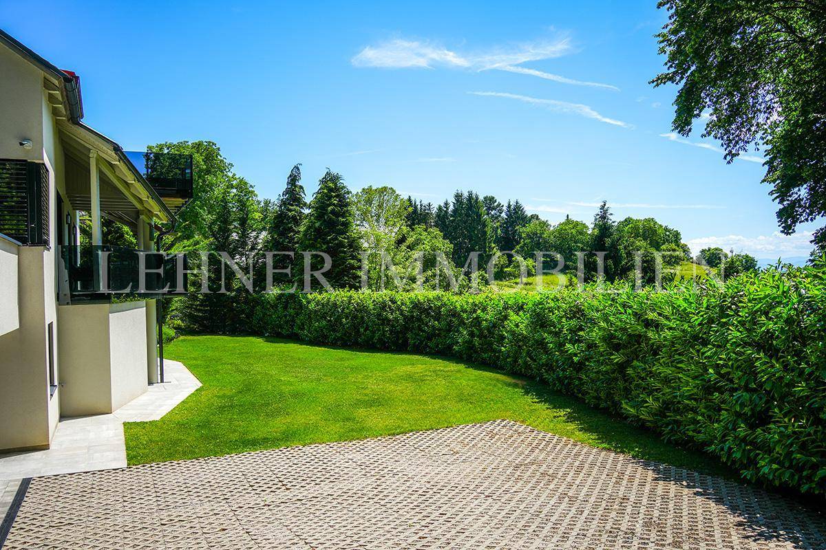 Gepflegte Rasenfläche neben dem Haus mit einer befestigten Fläche und Hecken.