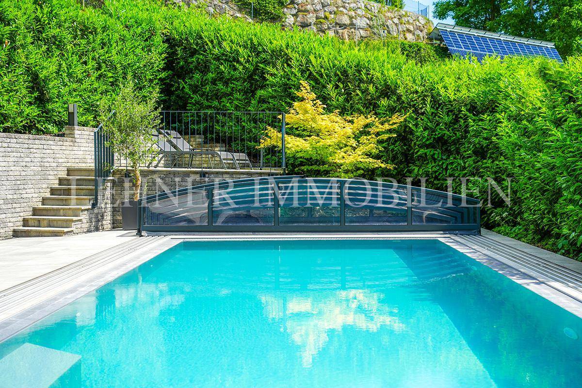 Swimmingpool mit Blick auf die grüne Hügellandschaft und Photovoltaikanlage im Hintergrund.