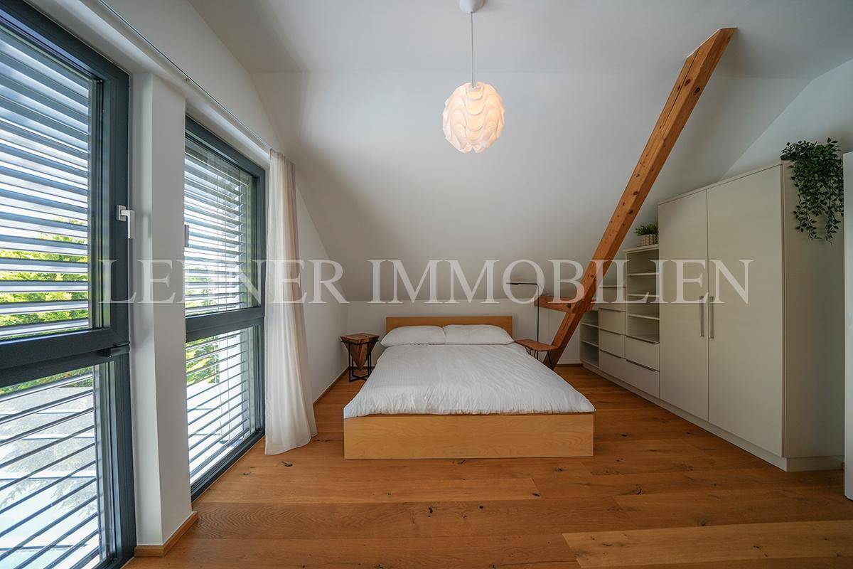 Gemütliches Schlafzimmer mit Holzboden, Dachschräge, großen Fenstern und integrierten Stauraummöglichkeiten.