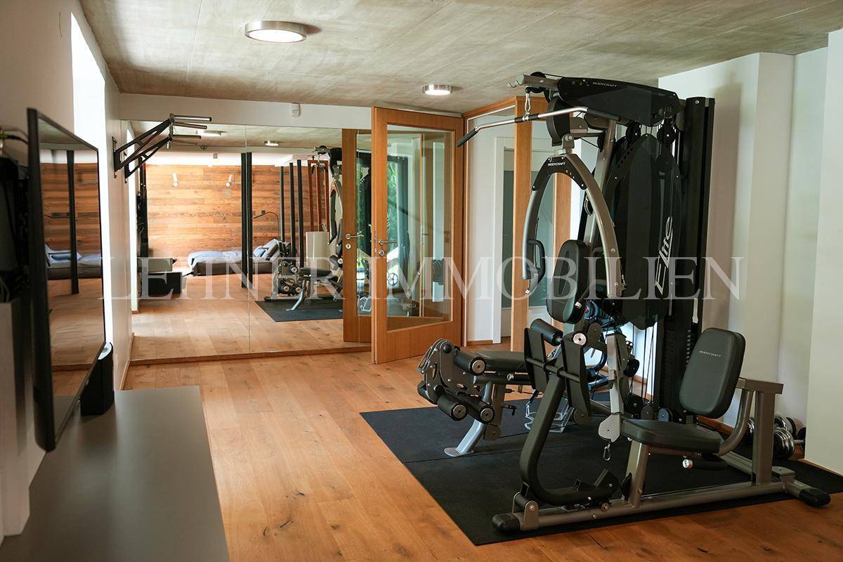 Fitnessraum mit Trainingsgeräten, Spiegelwand und Zugang zu einem weiteren Bereich.