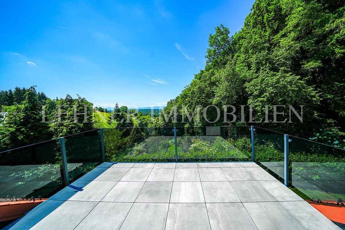 Große geflieste Terrasse mit Glasgeländer und weitem Blick über grüne Hügel und die Landschaft.