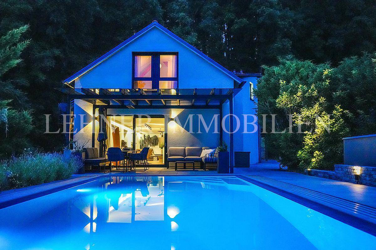 Beleuchteter Swimmingpool und überdachter Außenbereich mit Sitzgelegenheiten bei Nacht.