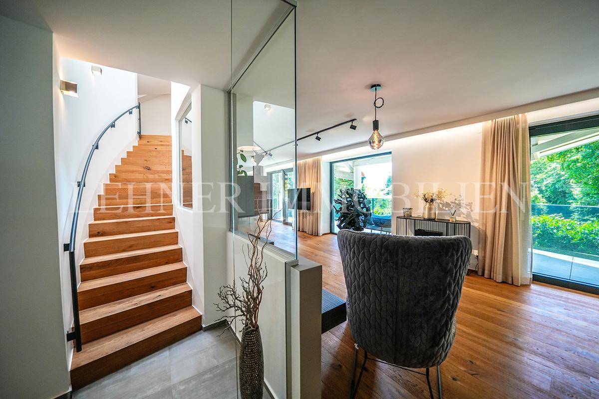 Heller Eingangsbereich mit eleganter Holztreppe und moderner Glasabtrennung zum Wohnbereich.