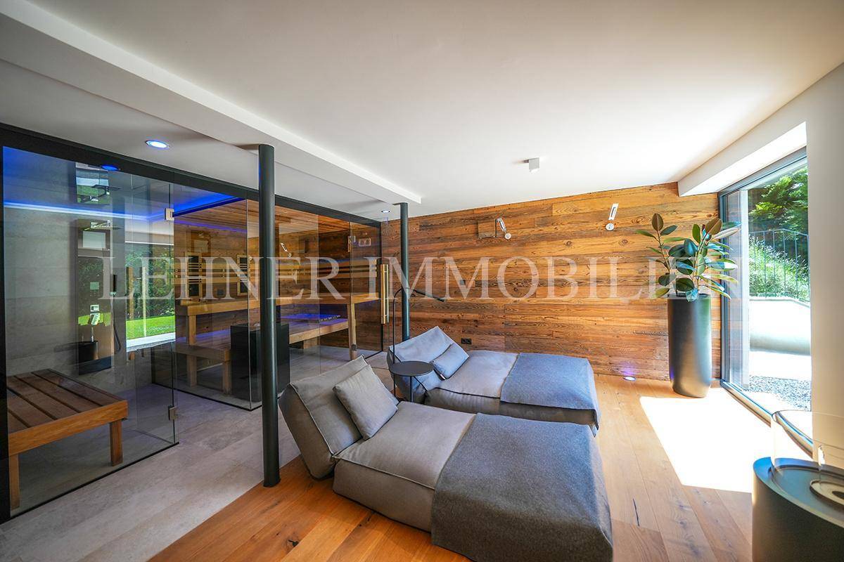 Entspannungsbereich mit Liegen, Holzwand und Blick auf die moderne Sauna und den Garten.