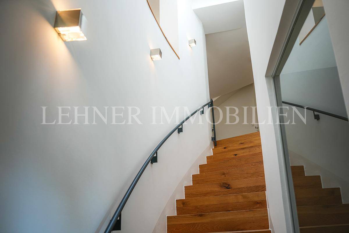 Detailaufnahme der Holztreppe mit modernem Geländer und stilvoller Wandbeleuchtung.