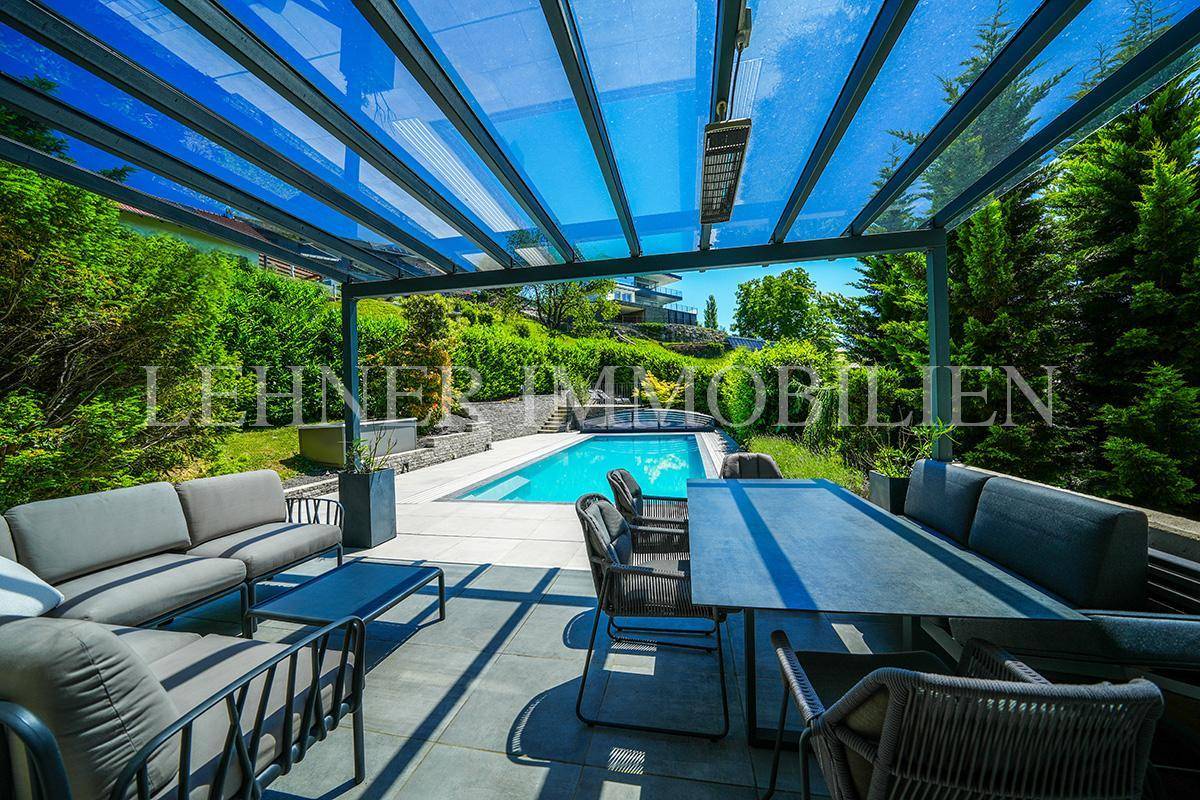 Großzügige Terrasse mit Glasüberdachung, bequemen Sitzmöbeln und Blick auf den Poolbereich.
