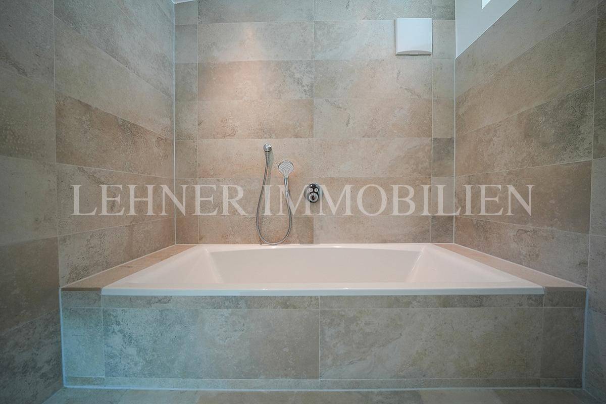 Eingebaute Badewanne in einem modernen Badezimmer, umgeben von großformatigen Fliesen.