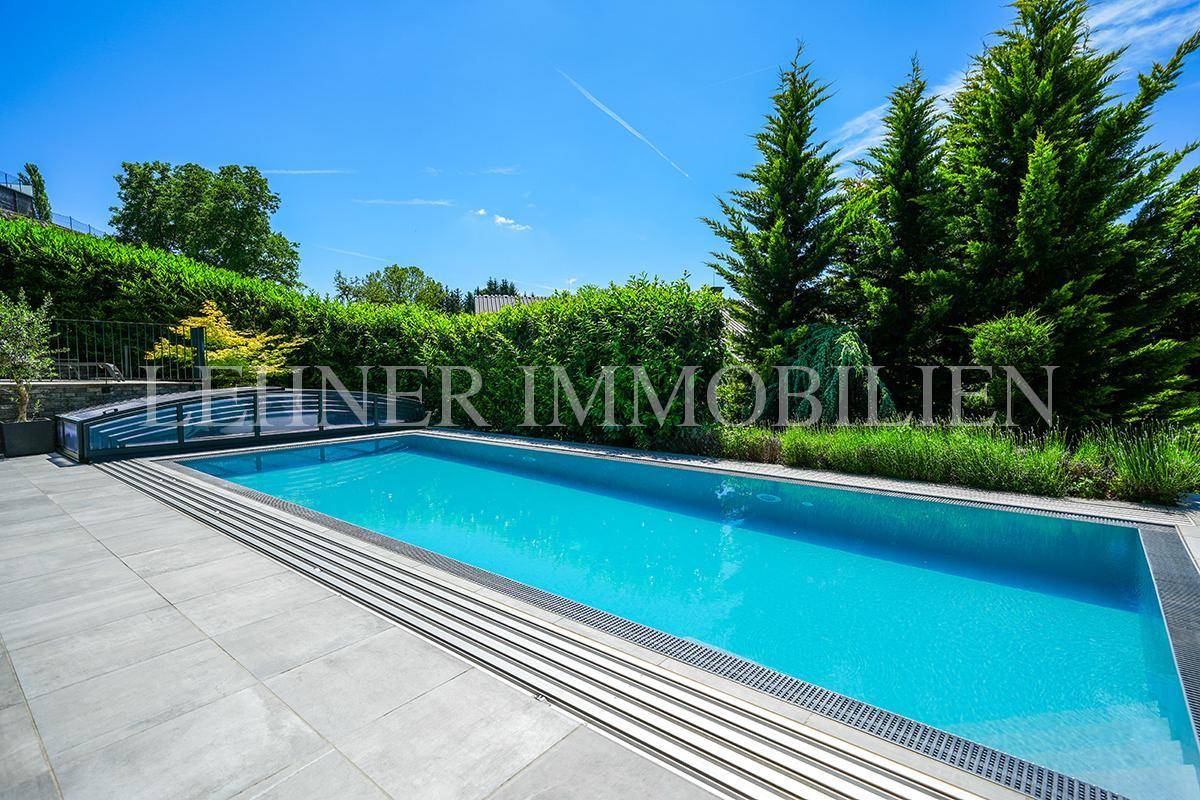 Langer Swimmingpool mit sauberer Poolumrandung und üppiger Heckenbepflanzung im Garten.