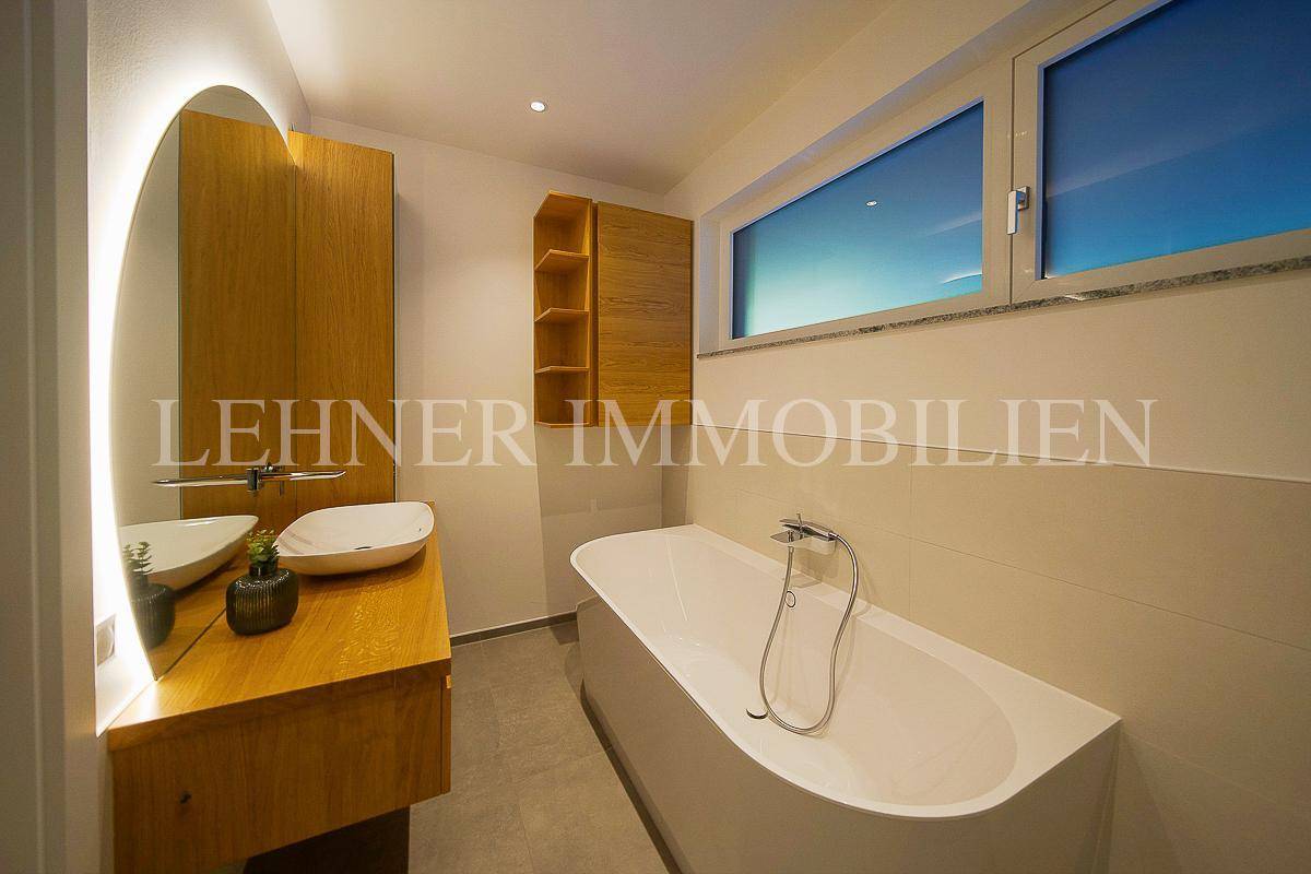 Helles Badezimmer mit Badewanne, Holzwaschtisch und Fenster, bietet eine angenehme Atmosphäre.