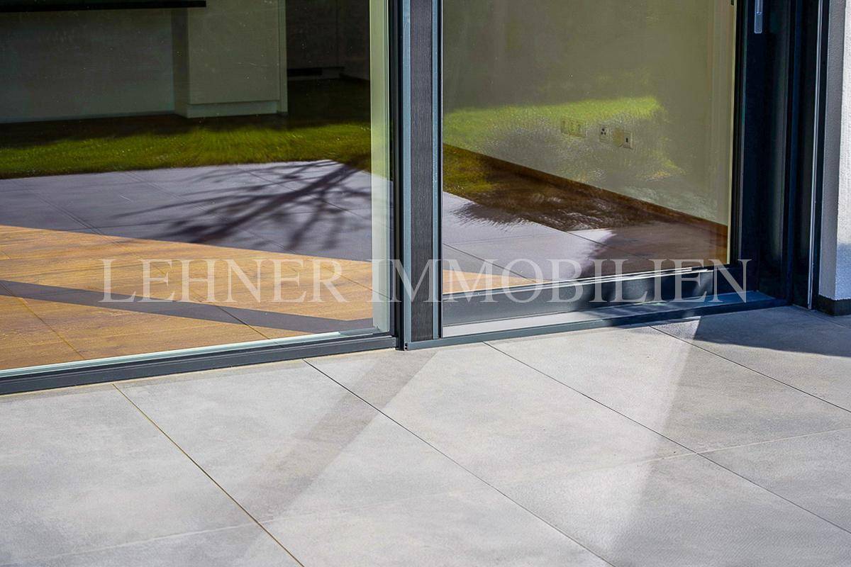 Detailansicht der Terrassenfliesen und der großen Glasschiebetür zum Innenbereich.