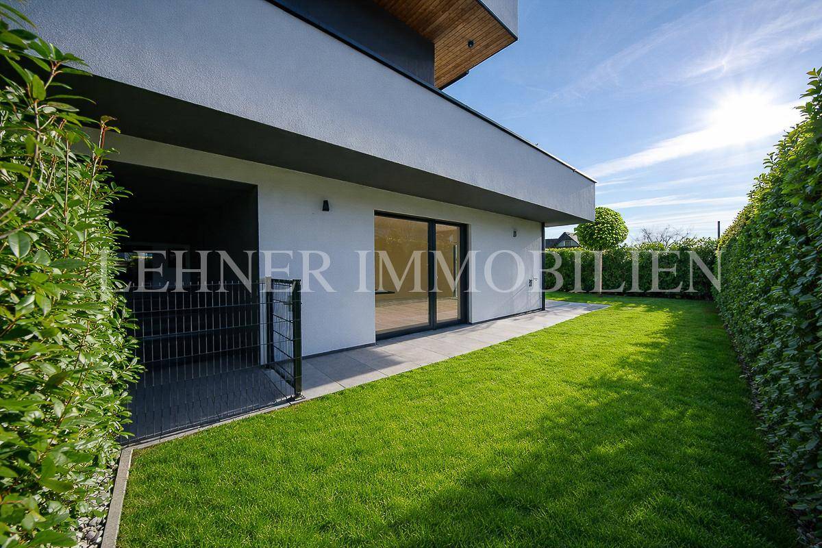 Seitlicher Gartenbereich mit Rasenfläche, Hecken und einem Zugangstor zum Haus.