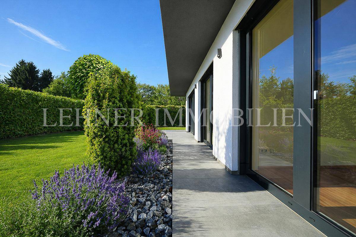 Seitlicher Zugang zum Haus mit gepflastertem Weg, Blumenbeeten und hohen Hecken.