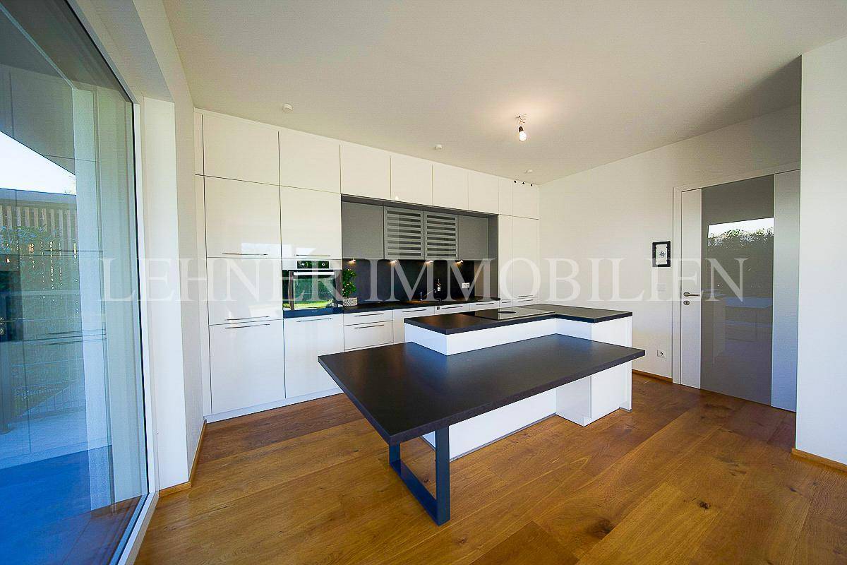 Moderne Einbauküche mit Kochinsel, dunklen Arbeitsplatten und Holzboden in offenem Wohnbereich.