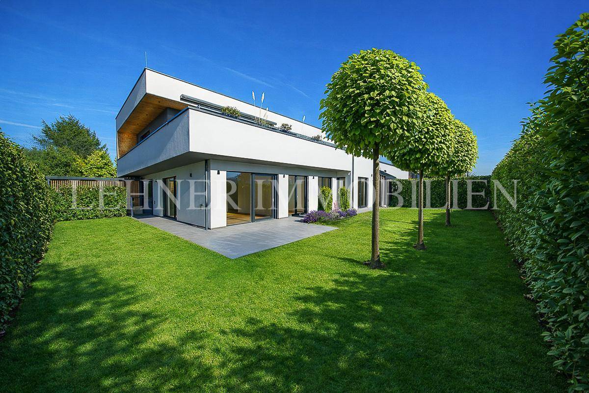 Modernes Haus mit gepflegtem Rasen, Hecken und Bäumen unter blauem Himmel.