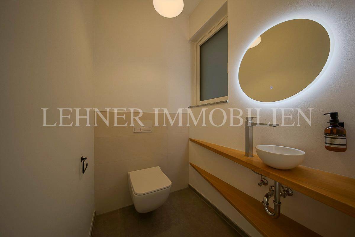 Modernes Gäste-WC mit wandhängender Toilette, Aufsatzwaschbecken und beleuchtetem Spiegel.