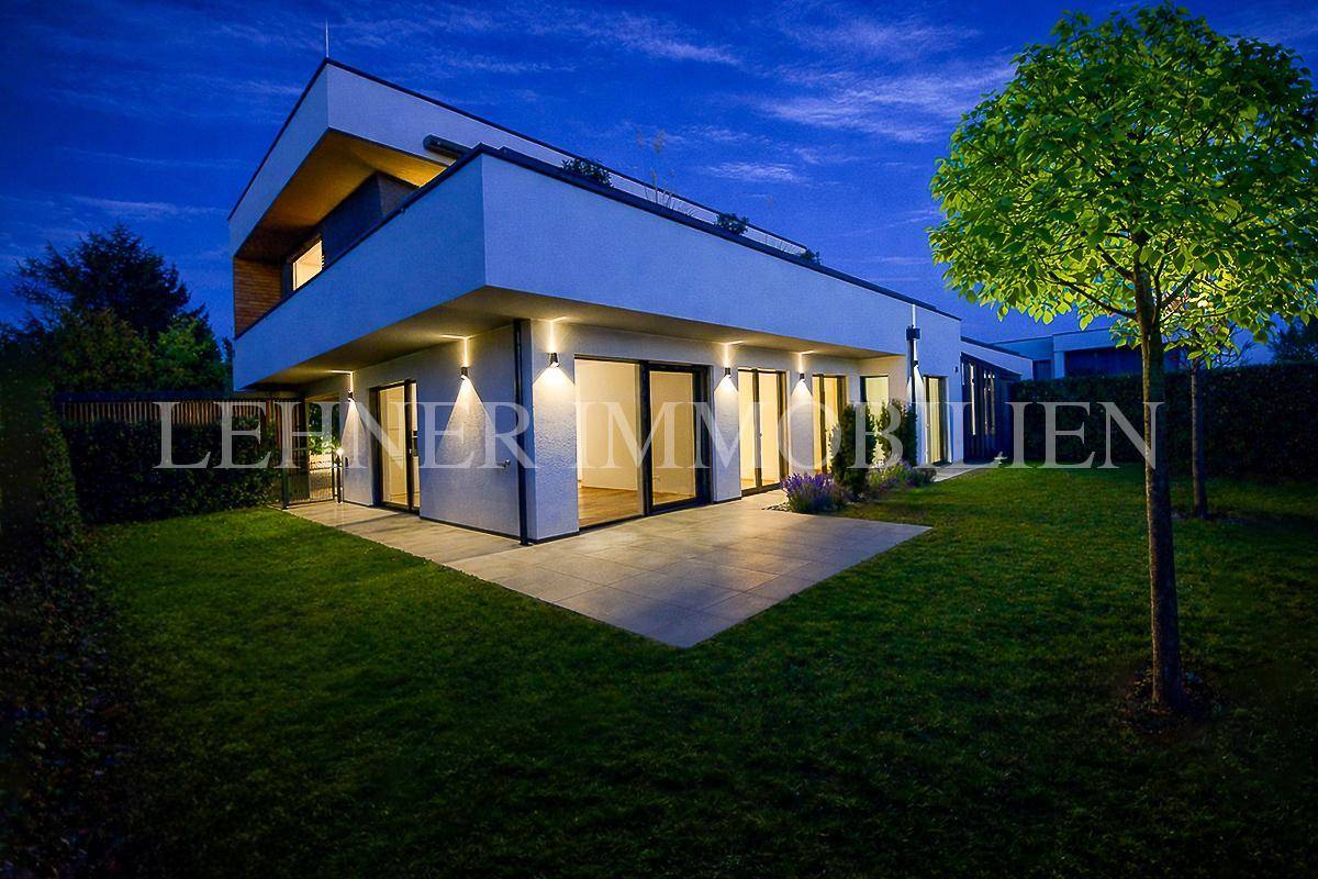 Moderne Architektur bei Nacht mit beleuchteter Terrasse und gepflegtem Rasen im Gartenbereich.