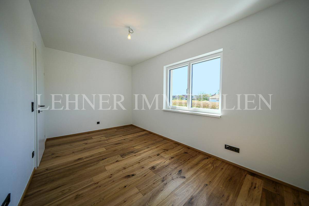 Geräumiges, unmöbliertes Zimmer mit Holzboden und großem Fenster für viel Tageslicht.
