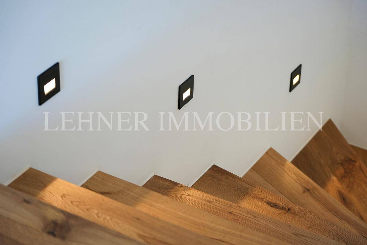 Detailansicht der Holztreppe mit eleganten, in die Wand eingelassenen Stufenleuchten.